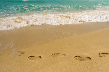 Turquoise sea water wave motion. Foot steps on sand. Calm sea. Seaside resort. Bright sky and waves on beach. Beautiful foamy shoreline. Sea background. Blue ocean. Sandy ocean beach. Sea waves.