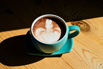 Close up view of hot chocolate with latte art in the green gauze cup. Wooden table, black, dark, shadow.