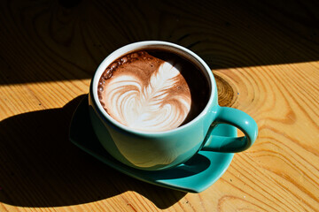 Close up view of hot chocolate with latte art in the green gauze cup. Wooden table, black, dark, shadow.