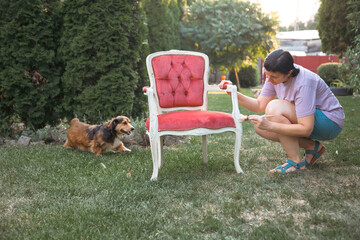 Woman painting a wooden furniture while sitting with her dog in the garden. DIY concept.