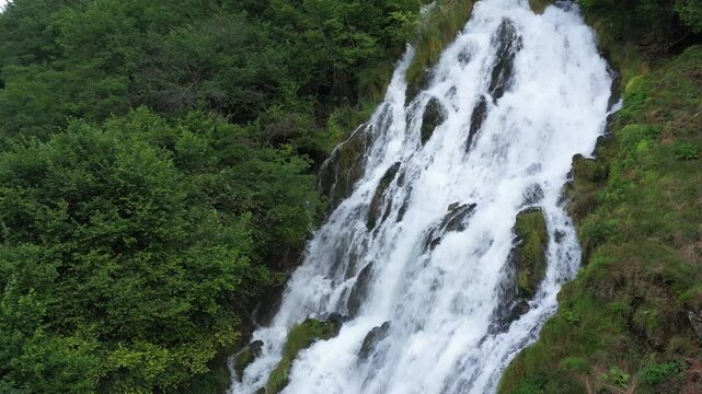 Nature's Symphony: Summer Waterfall Surrounded by Green Grass and Bushes