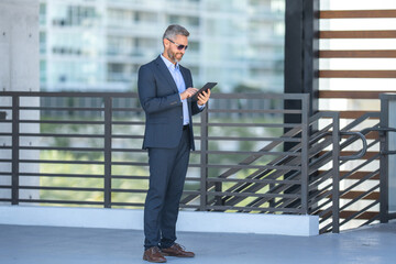 Successful businessman outdoors with tablet. Confident businessman using tablet outside. Mature businessman entrepreneur checking finance data. Rich businessman banker reviewing contract on tablet.