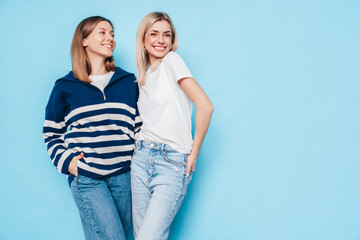 Naklejka premium Two young beautiful smiling brunette hipster female in trendy summer clothes. Lovely women posing on blue background in studio. Positive models having fun. Cheerful and happy. isolated