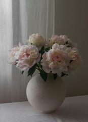 A bouquet of white peonies in a ceramic vase on a table with a white tablecloth in the living room