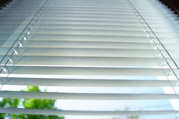 Obraz premium Interior pattern: horizontal stripes of open blinds photographed from bottom to top. Options for protecting an apartment from sunlight: pleated blinds. Background with an everyday item.