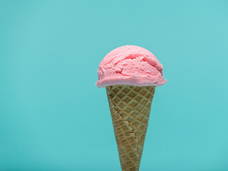 A single scoop of pink ice cream sits atop a crispy waffle cone on a vibrant turquoise backdrop