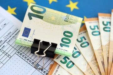 European euro currency money notes bunch on tax form and European union blue flag close up