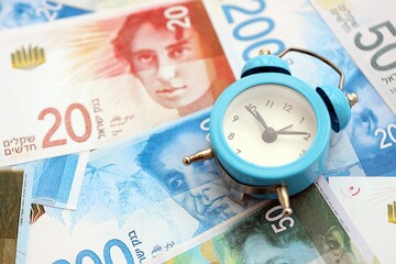 Israel New Shekels banknotes and alarm clock. The current Israel money bills and clock lies on table