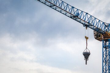Industrial crane lifts concrete bucket at construction site with cloudy sky in background