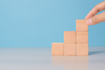 Man's hand organizing wooden blocks on blue surface. Symbolizes workflow, step-by-step strategy, or structure