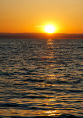 Obraz premium The sun is setting over the ocean, casting a warm glow on the water