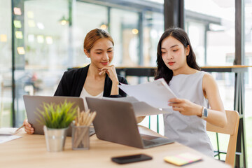 Two asian business women in teamwork discussing and using laptop in the office . Two excited happy asian business women are talking and consulting.
