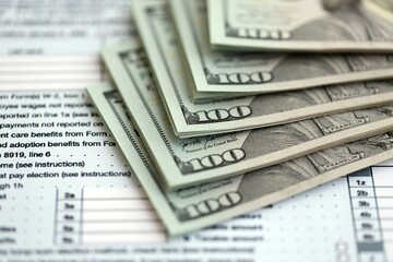 Big amount of United States USD dollar bills banknotes on table with 1040 tax return form