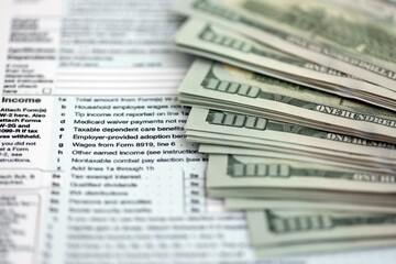 Big amount of United States hundred dollar bills in bunch on table with tax return form