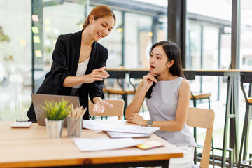 Two professional caucasian asian business women friends collaboration, working together at office,...