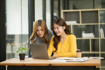 Two Asian businesswomen using laptops, on the table there are graph documents working on business investment.