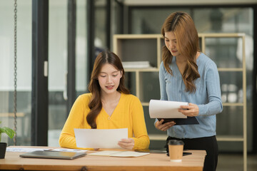 Asian businesswoman sitting in a meeting, talking about a document and chart placed on the table.
