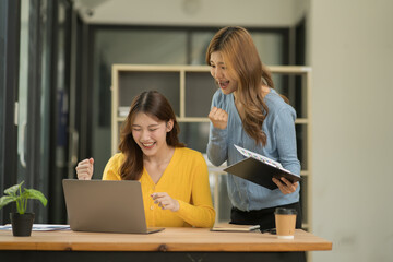 Two Asian businesswomen using laptops, on the table there are graph documents working on business investment.