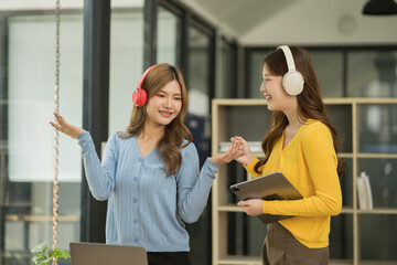 Asian woman wearing headphones standing and dancing celebrating, showing her appreciation, joy, office room