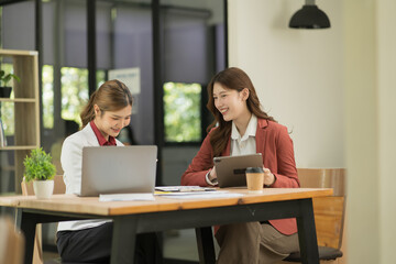 Two Asian businesswomen using laptops, on the table there are graph documents working on business investment.