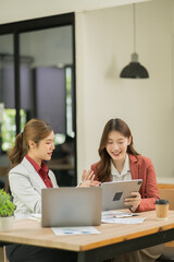 Two Asian businesswomen using laptops, on the table there are graph documents working on business investment.