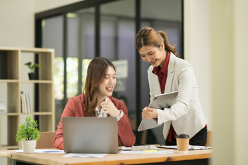 Two Asian businesswomen using laptops, on the table there are graph documents working on business investment.
