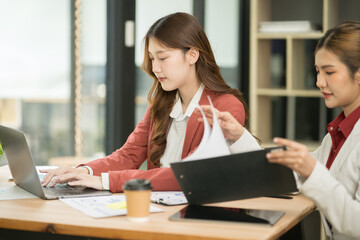 Two Asian businesswomen using laptops, on the table there are graph documents working on business investment.