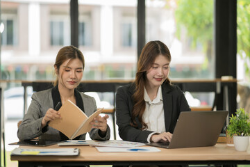 Two Asian businesswomen using laptops, on the table there are graph documents working on business investment.