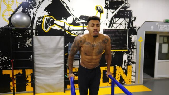 Strong african man doing push ups on parallel bars at sport club. Muscular afro american sportsman with tattoos doing hard exercises modern gym. Concept of healthy and active lifestyle. Slow motion