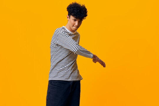 young man in striped shirt posing with playful expression against bright yellow background, casual style, modern fashion, confident attitude