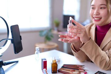 Asian Woman Reviews Beauty Serum on Video Stream for Online Makeup Tutorial and Cosmetic Product Demonstration in a Home Studio
