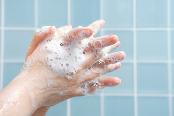 Fototapeta premium The woman washes her hands with foam against blue tiles background in bathroom side view close-up.