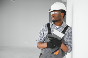 business, building, and people concept. african builder in hardhats with plastering tools indoors