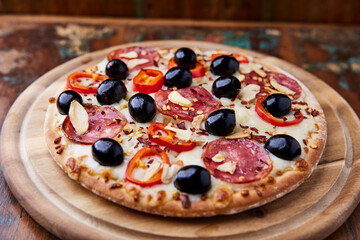 Pizza with salami and mozzarella cheese, jalapeno pepper and black olives. Wooden background. Soft focus. Close up.	