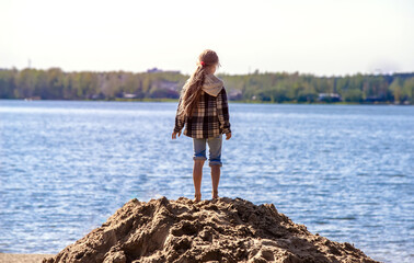 A girl stands on the sand against the background of the sea