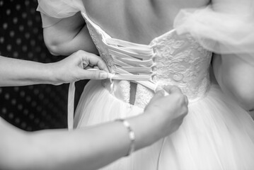 The girl laces up the corset on the bride's dress
