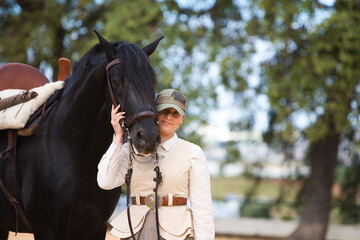 Young and beautiful woman holds with affection the face of her black purebred Spanish horse and...