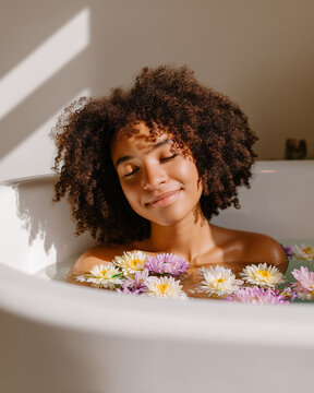 Woman enjoying a relaxing bath surrounded by colorful flowers in a bright, serene bathroom