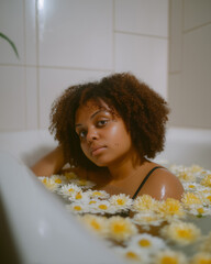 Young woman relaxing in bathtub filled with flowers in serene indoor setting during evening