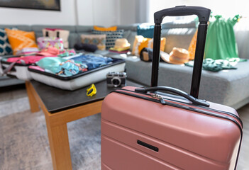 Pink suitcase stands ready for a journey, while another suitcase lies open on a table, overflowing with colorful summer clothes, evoking the excitement of upcoming travel and vacation