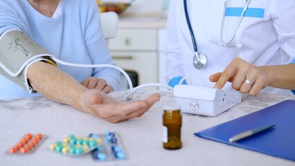 Female doctor measuring blood pressure of a senior woman during a home visit, with pills and a...