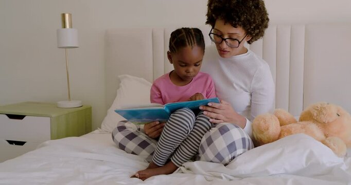 Mother and daughter bonding as child opening blue picture book, guiding reading and giggling on bed