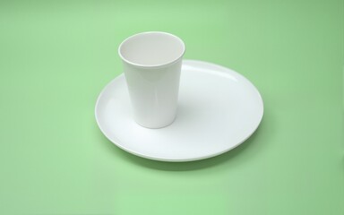 White minimalism with plate and plastic cup on green background. Essential and balanced composition, ideal for design, consumption, single-use waste or environmental sustainability themes