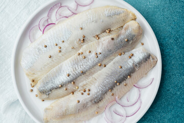 Marinated herring fillets with coriander seeds, onion and herbs on white plate with napkin over blue background