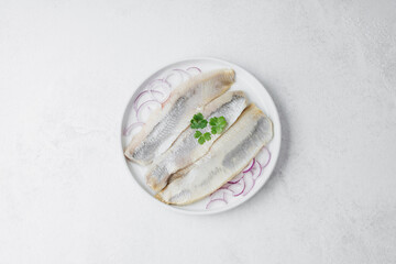 Marinated herring fillets with red onion and parsley on white plate over light background