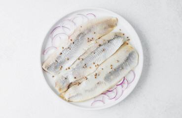 Marinated herring fillets with red onion and parsley on white plate over light background