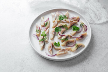 Marinated herring slices with red onion and herbs on white plate over light background