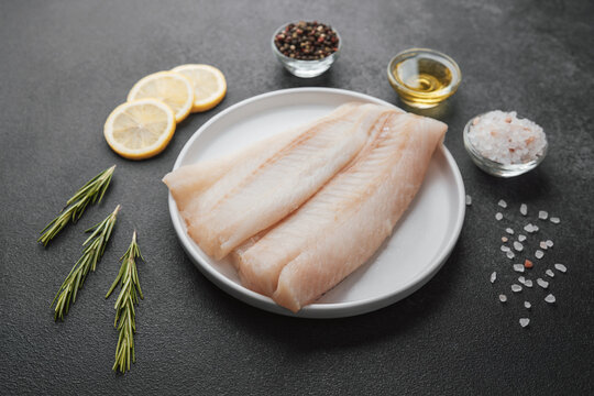 Raw pollock fillet with spices, lemon and rosemary on dark background