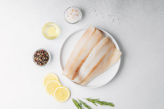 Raw pollock fillet with lemon and rosemary on white background