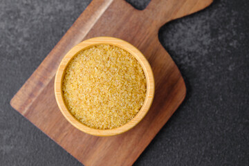 Cracked wheat groats in wooden bowl on black background. Healthy raw cereal grains.